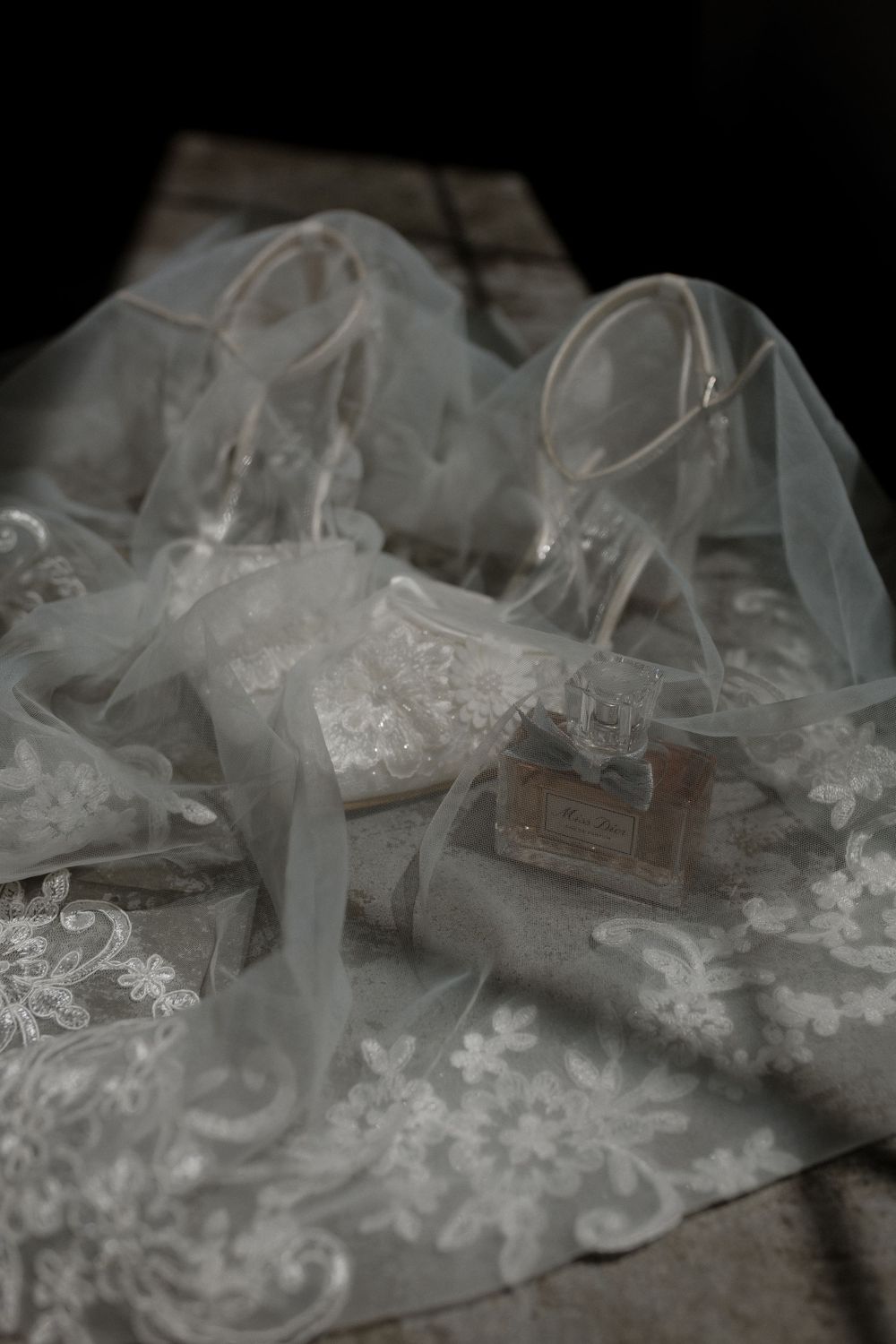 Delicate lace wedding shoes displayed on embroidered fabric in dramatic lighting.