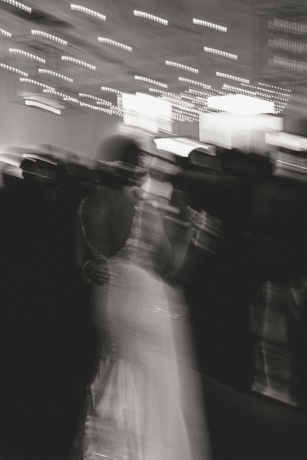 Abstract black and white motion blur of dancers at a reception with overhead lights.