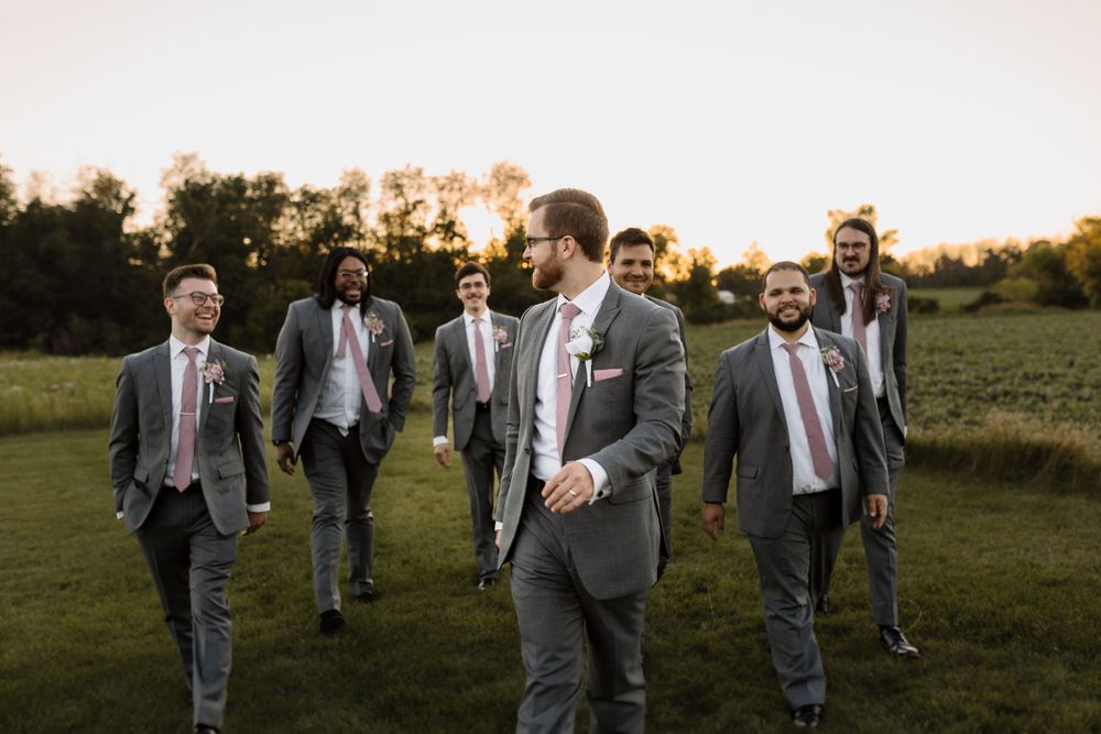 Groomsmen walking across a grassy field at sunset in matching grey suits.