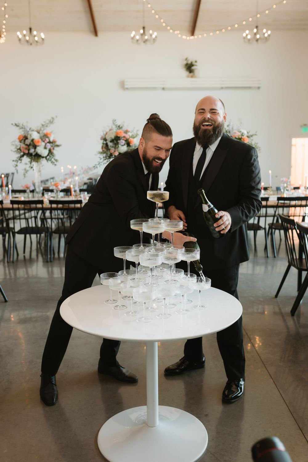 Two men in black suits setting up a champagne tower at an elegant wedding reception venue.