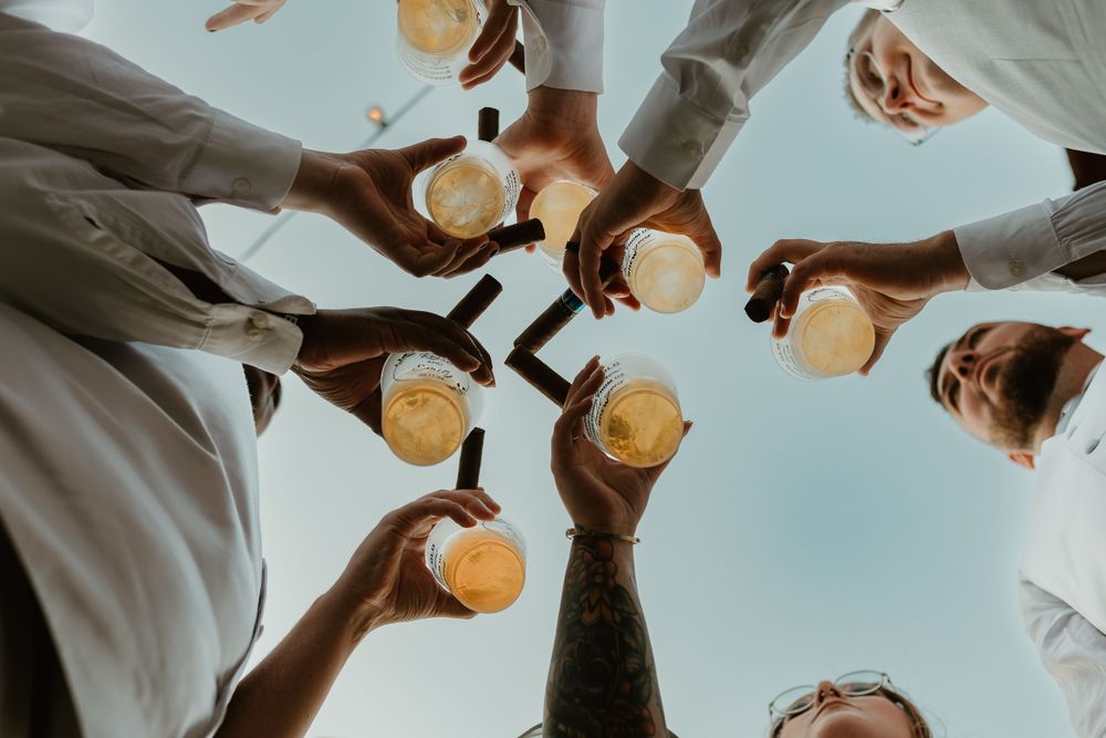 Friends toasting with drinks against a bright sky in a celebratory circle.