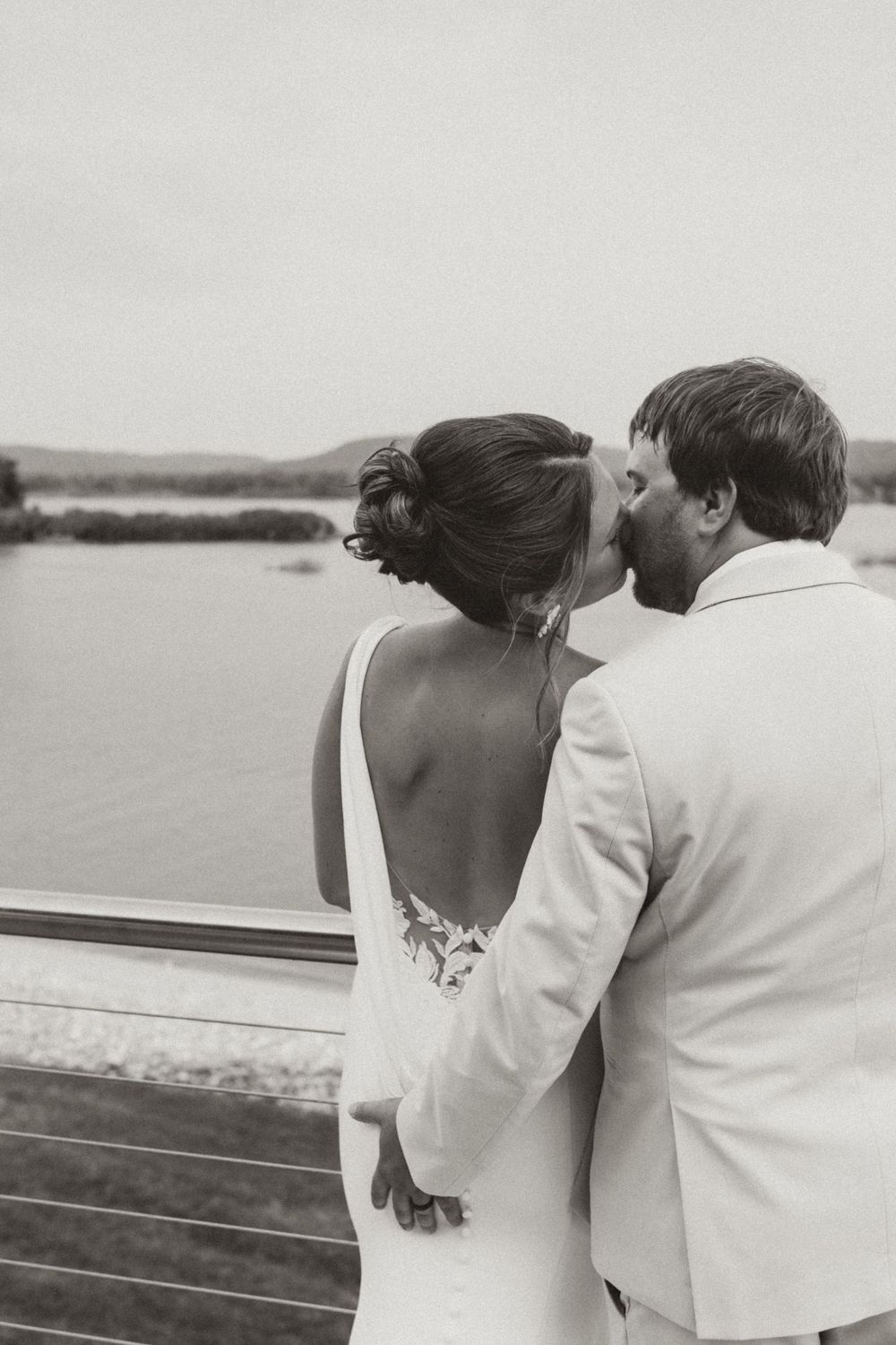 Romantic black and white photo of a couple in wedding attire looking out over water.