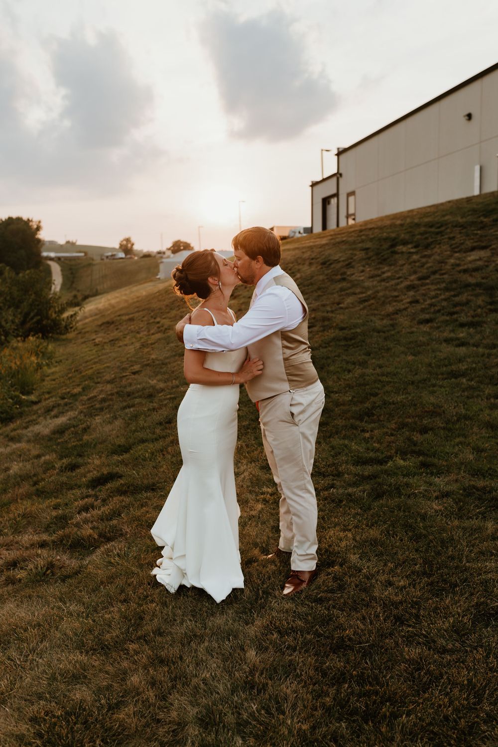 Newlywed couple embraces on a hillside during golden hour.