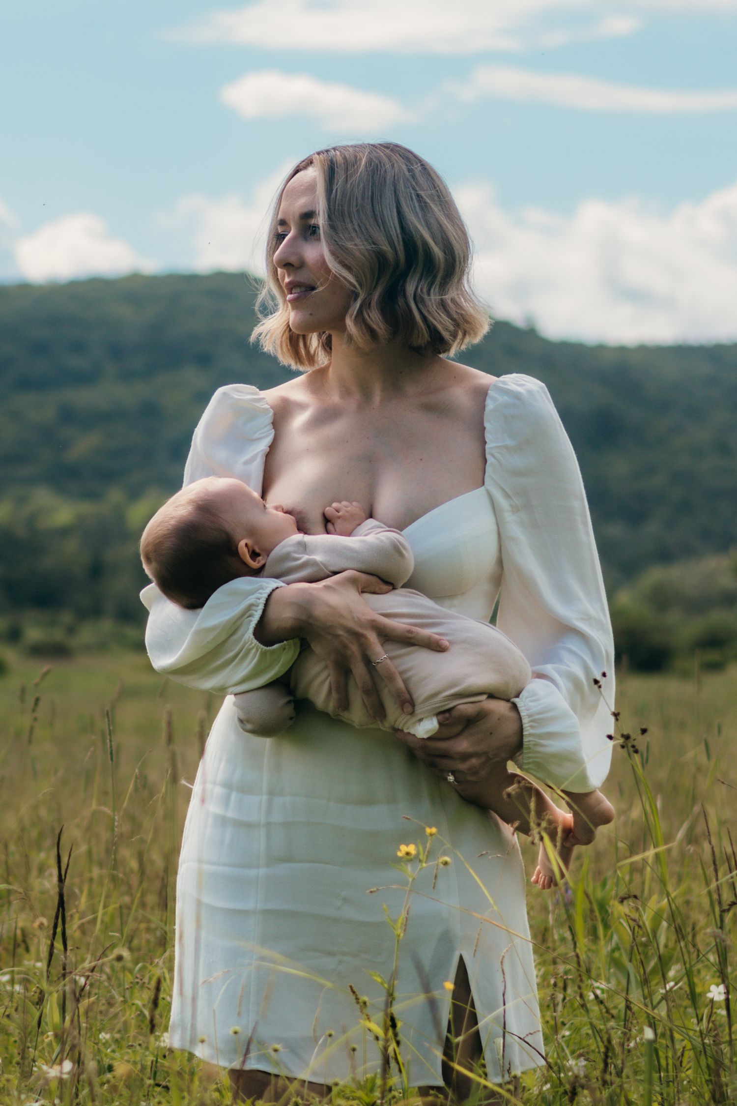 A woman standing in a field nursing her baby