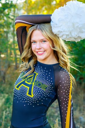 Close up of cheerleader in navy uniform with sparkly details and white pom poms.