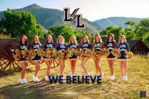 Cheerleading team in navy uniforms poses in formation with mountains and rustic wagon in background.