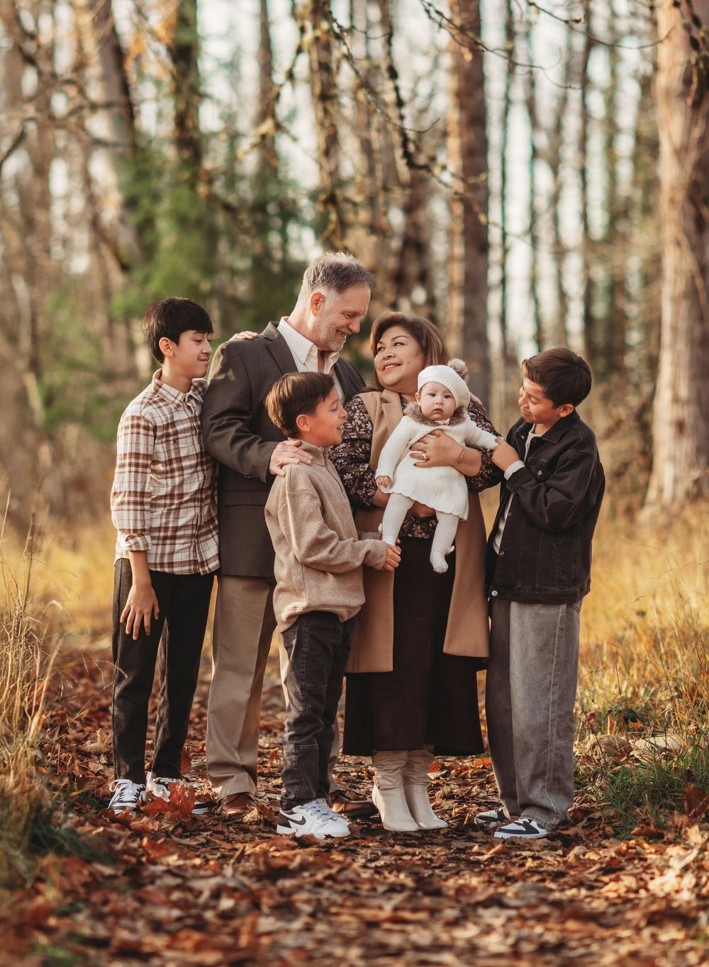 A group of people stand together in a wooded autumn setting with fallen leaves on the ground.