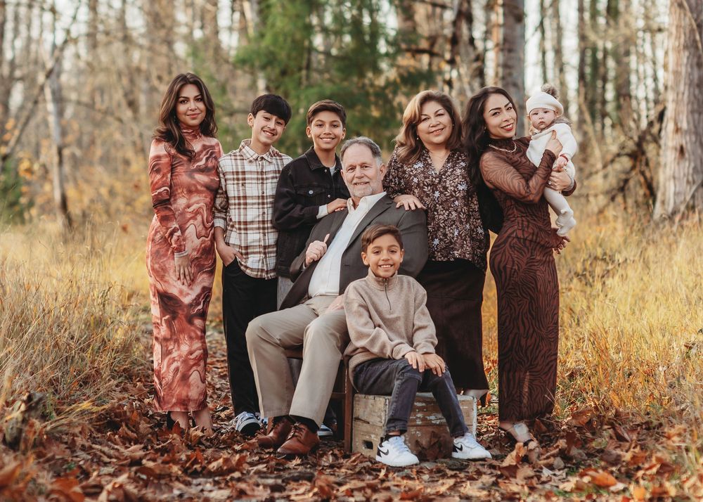 A group of people sitting together outdoors in autumn foliage wearing coordinated earth-toned clothing for a family photo.