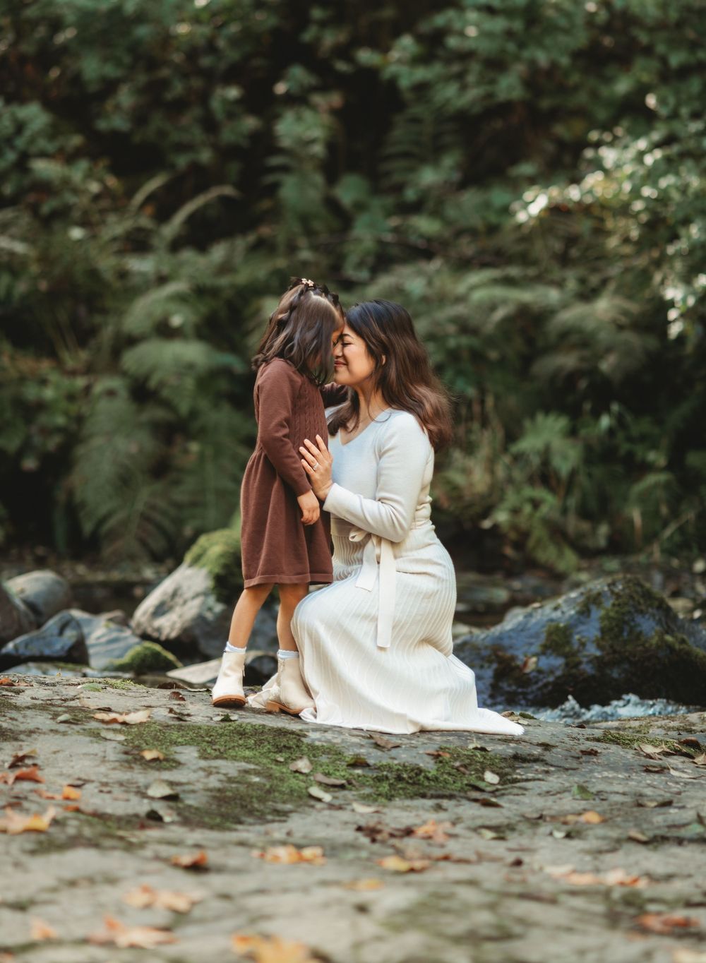 A couple sits together on a rocky riverbank surrounded by autumn foliage and shares intimate moments in nature.