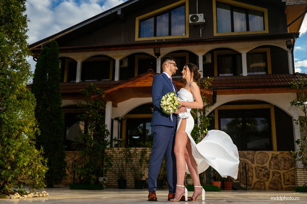 A romantic moment captured in front of a beautiful stone and wood mansion with sunlight streaming through on a bright day.