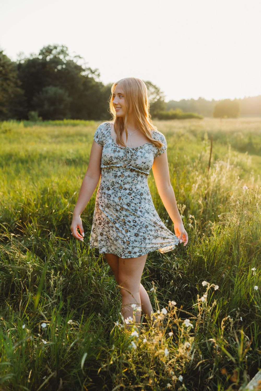 Person in floral dress walking through golden wildflower field at sunset.