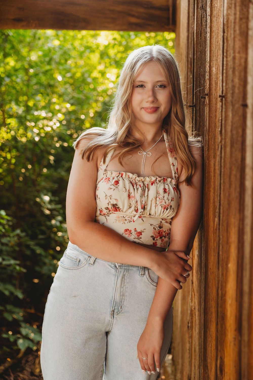 Portrait series of woman in floral top and light jeans posing against wooden background.