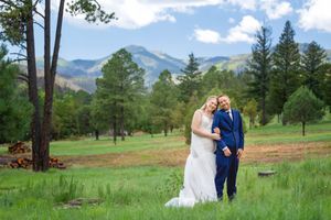 Smiling bride and groom posing together in a green meadow surrounded by pine trees and mountains in Ruidoso, NM.