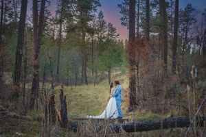Romantic couple sharing a kiss in a pine forest at dusk, bride in flowing white gown.