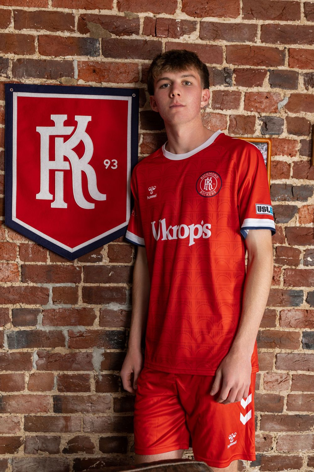 Red brick wall display with sports team logos and jerseys.