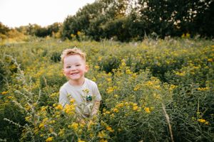 A young child stands joyfully in a field of yellow wildflowers on a sunny day.