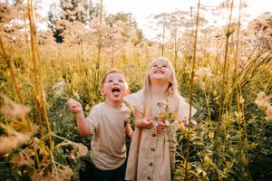 Two people share genuine laughter while standing among tall flowering plants at sunset.