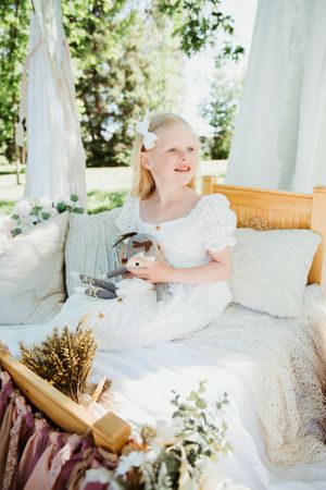 Child in white dress seated at outdoor tea party with vintage decor and floral arrangements.