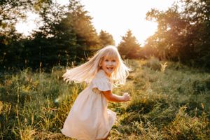 A white dress twirls through a sunlit meadow during golden hour.