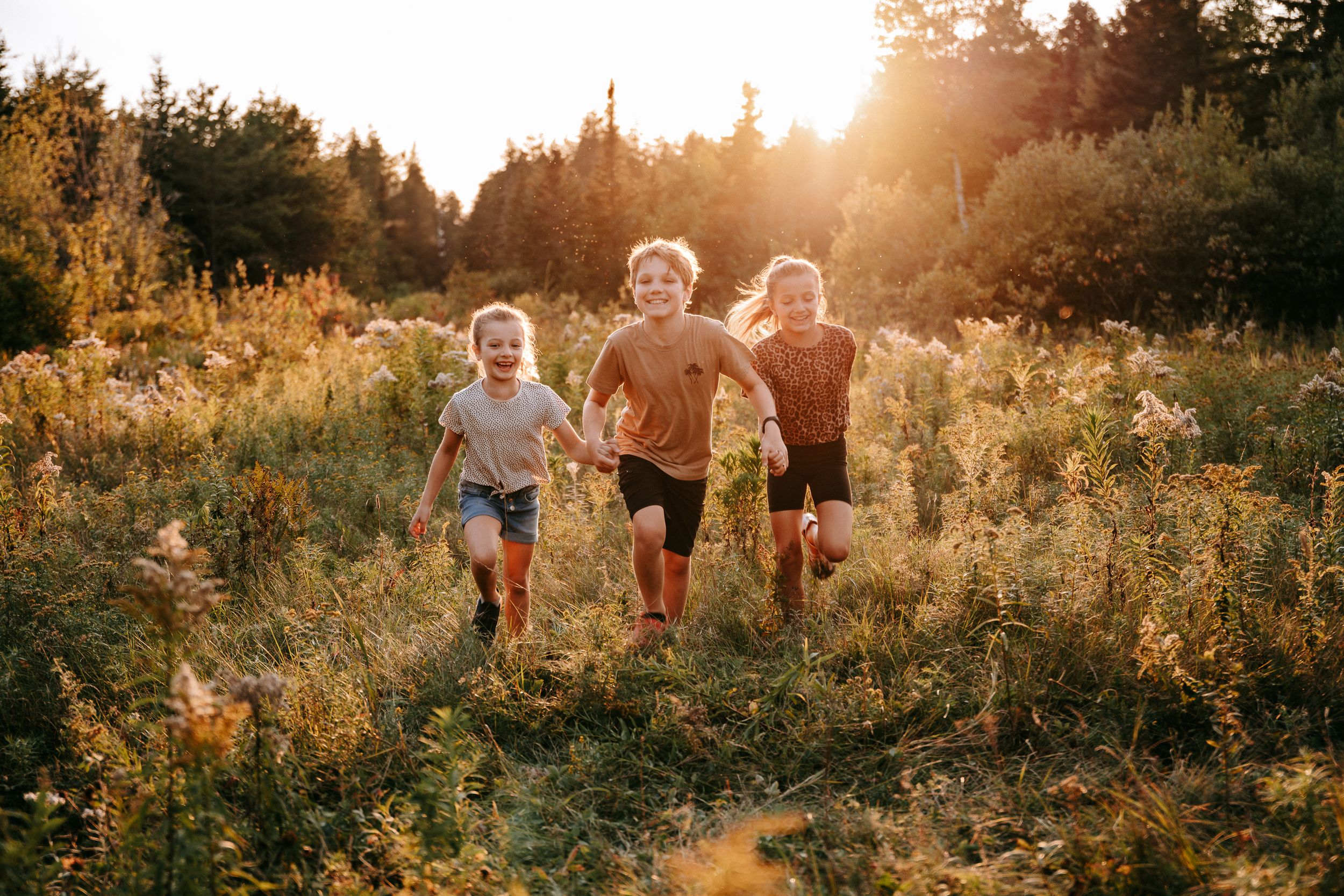 Family running through a sun-drenched wildflower meadow at golden hour.