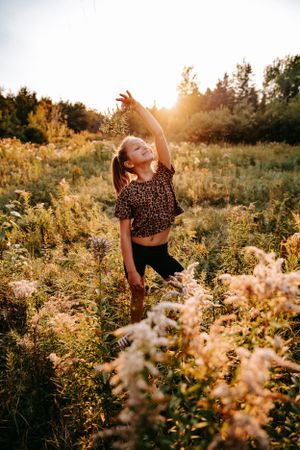 Young person dancing freely in a wildflower field during sunset.