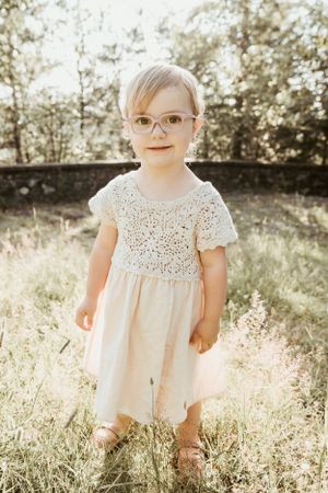 A sweet portrait in a lace dress and glasses standing in golden sunlight.