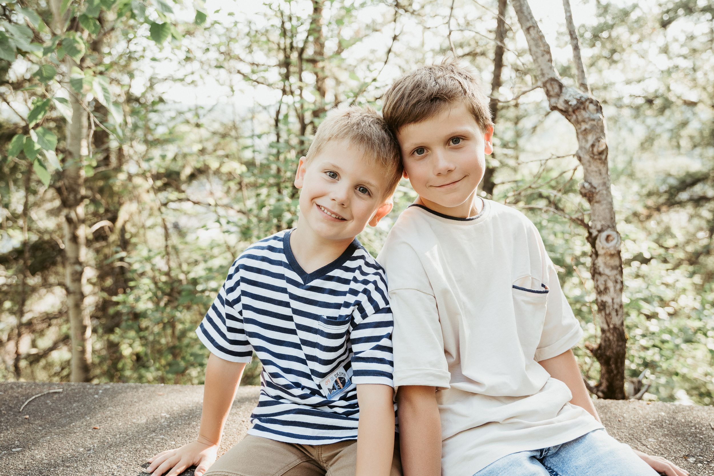 Two people sit close together outdoors wearing casual summer clothing.