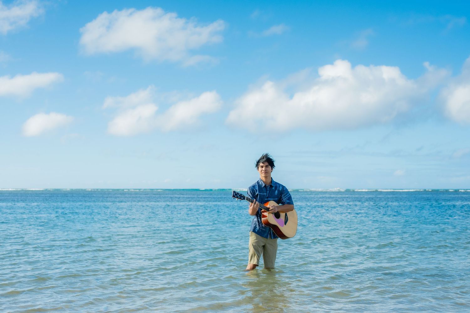 Hawaii senior standing in ocean holding his guitar