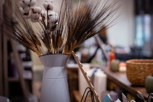 A collection of natural fiber dusters and brushes displayed in white ceramic vases on a wooden surface.