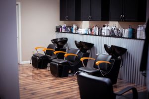 Black leather massage chairs line up against a wall in a spa treatment room with wooden flooring.