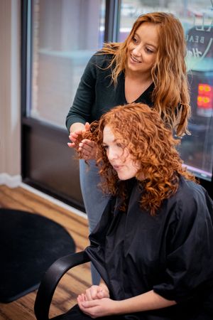 A hairstylist works on styling beautiful curly red hair in a salon setting.