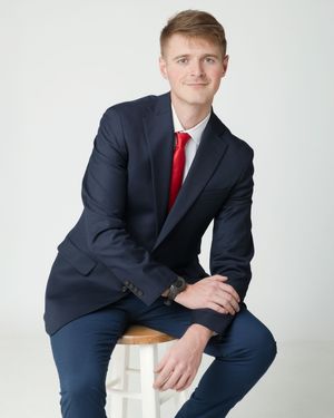 Professional seated poses in a navy suit and red tie against white studio backdrop.