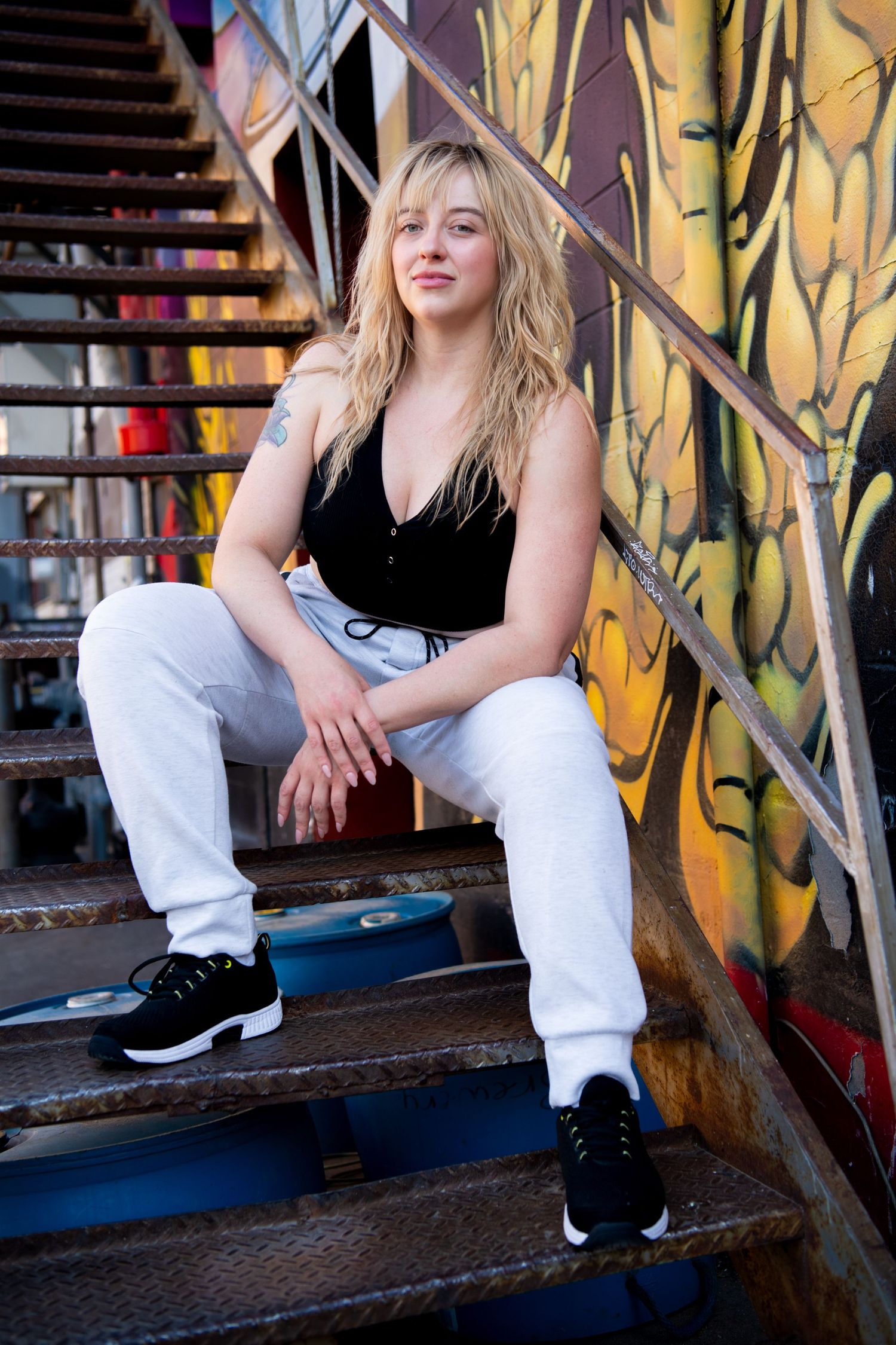 Urban fashion portrait against colorful graffiti wall with black sneakers and white sweatpants in casual street style.