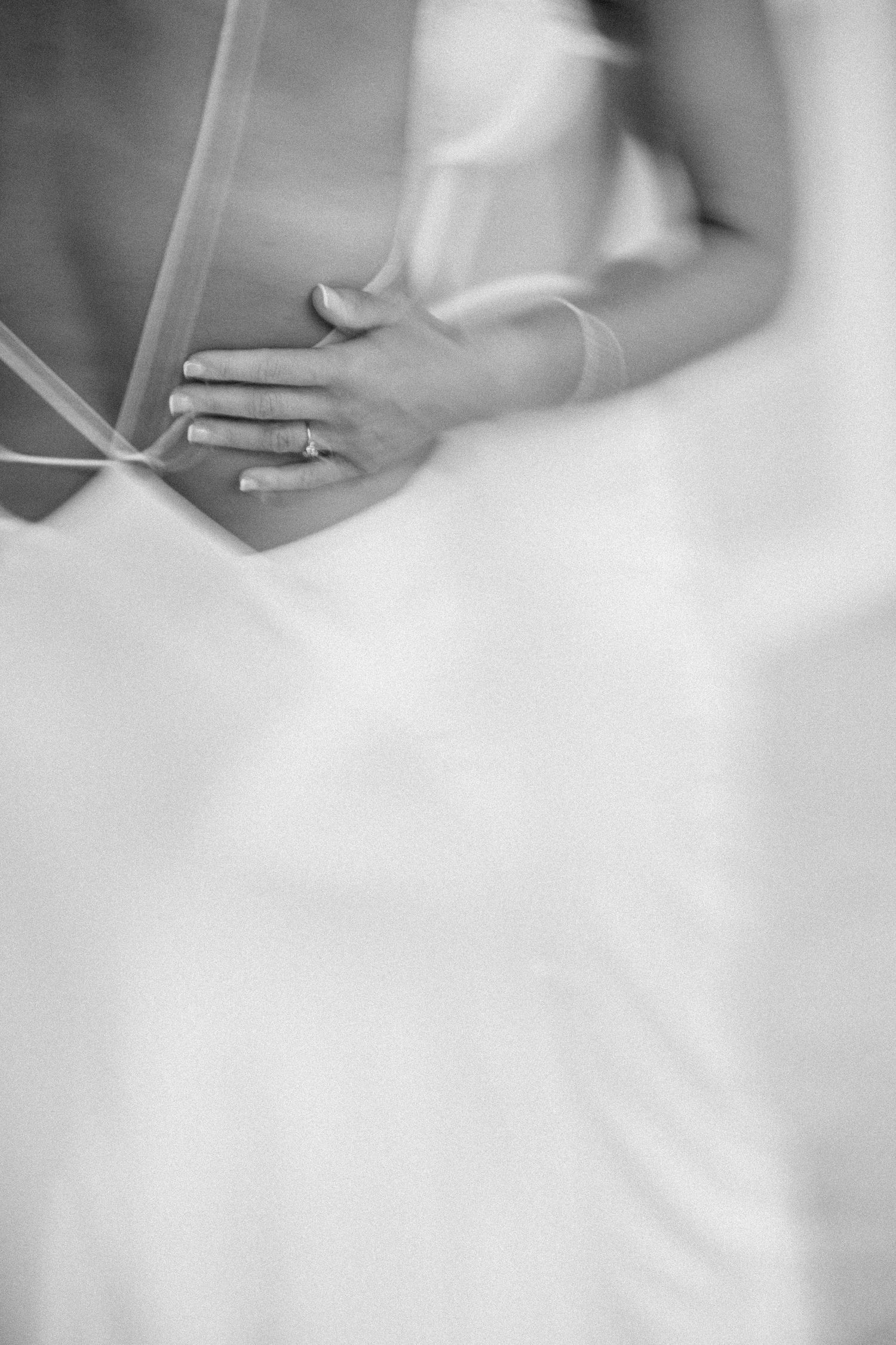 Black and white photo of a bride in a white gown, her hand resting on her waist, adorned with a diamond ring.