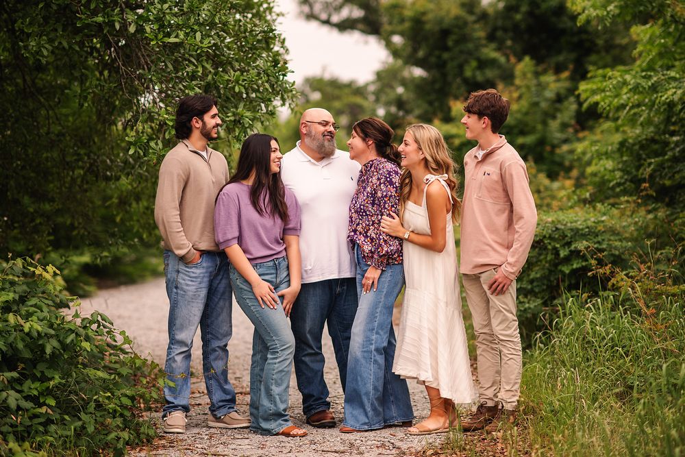 Family of six smiling together on a lush green tree-lined path outdoors.