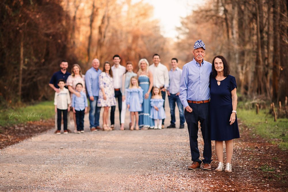 Large extended family group portrait on a tree-lined dirt road during golden hour.