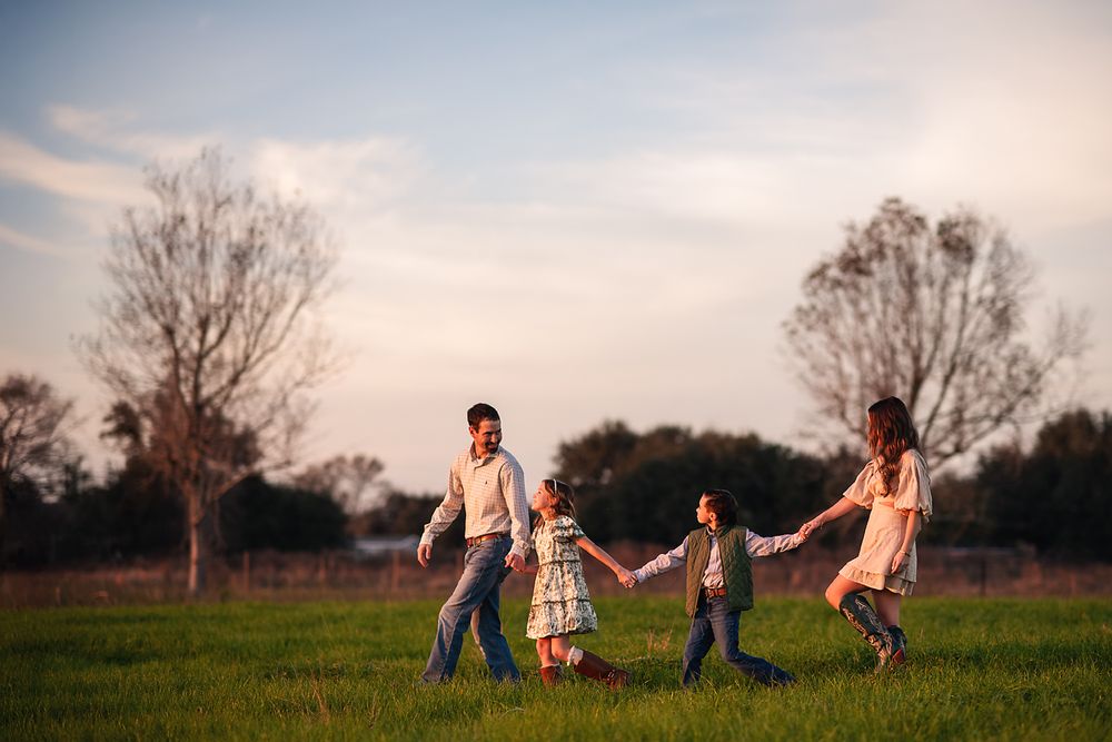 Happy family holding hands walking in green field at sunset.