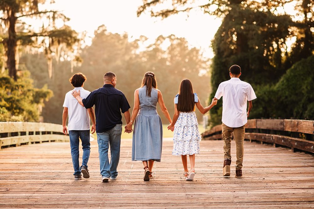 Family of five walking hand-in-hand on a wooden bridge at golden hour sunset.
