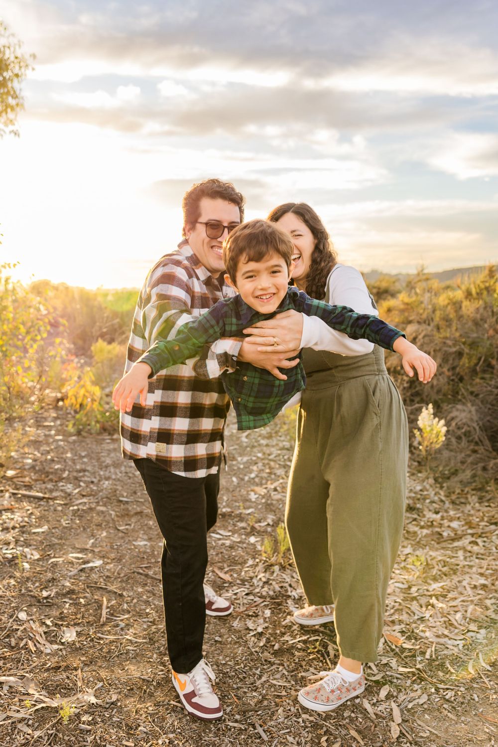 San Diego Photographer. A family plays and laughs together on a hilltop trail during golden hour sunset with mountains in the background.