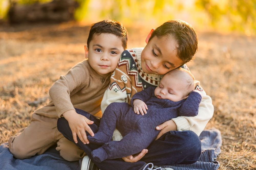Family members share tender moments together while sitting on autumn leaves at sunset.