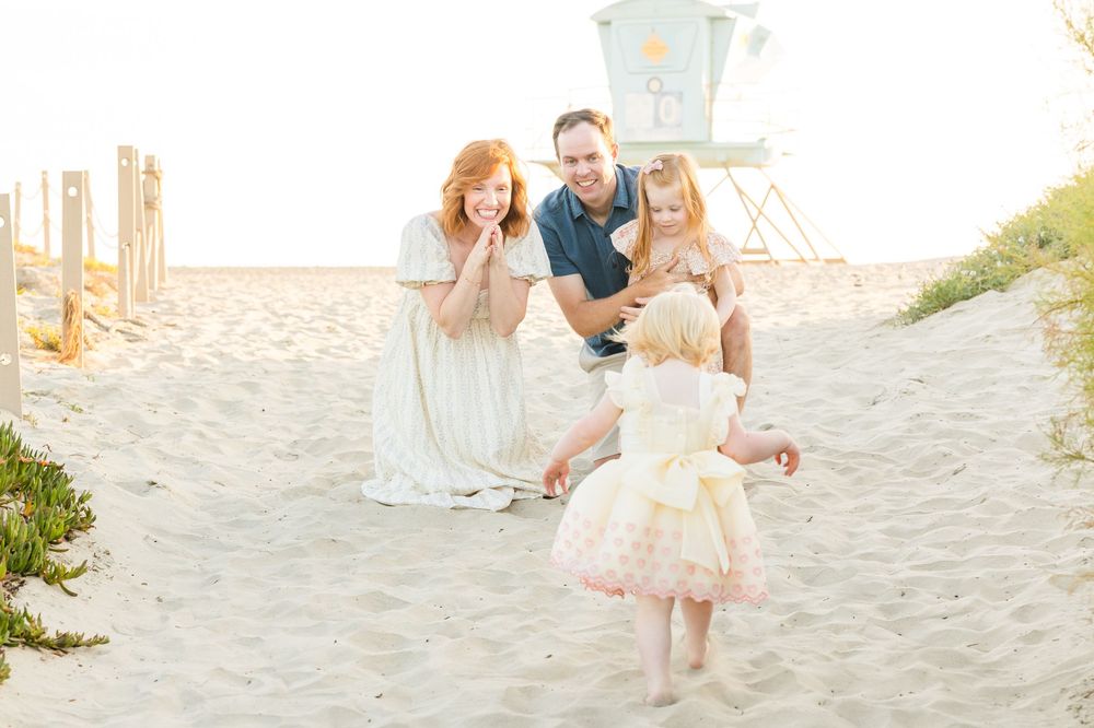 A family sitting together and laughing on a sunny beach with a lifeguard tower in the background.