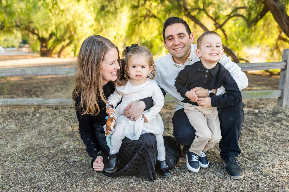 A family sits together outdoors on a sunny day surrounded by trees in a natural setting.