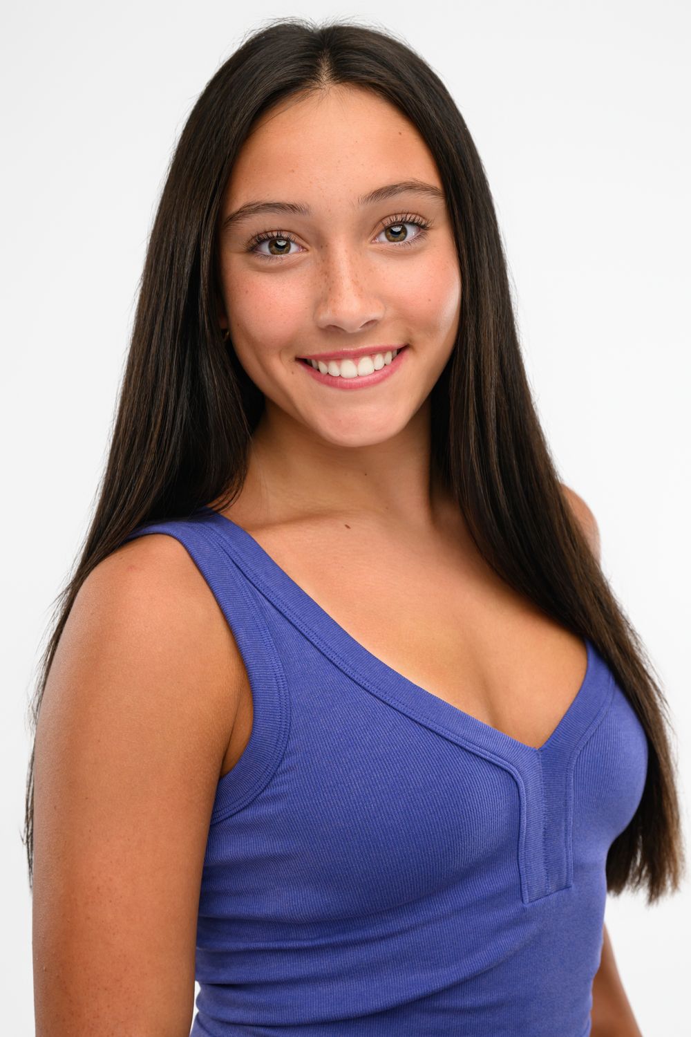 Smiling young woman with long dark hair wearing a blue sleeveless top against a white background.
