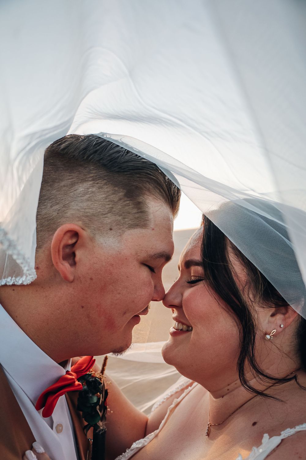 A romantic wedding moment captured under a flowing white veil against a soft background. Wedding photography