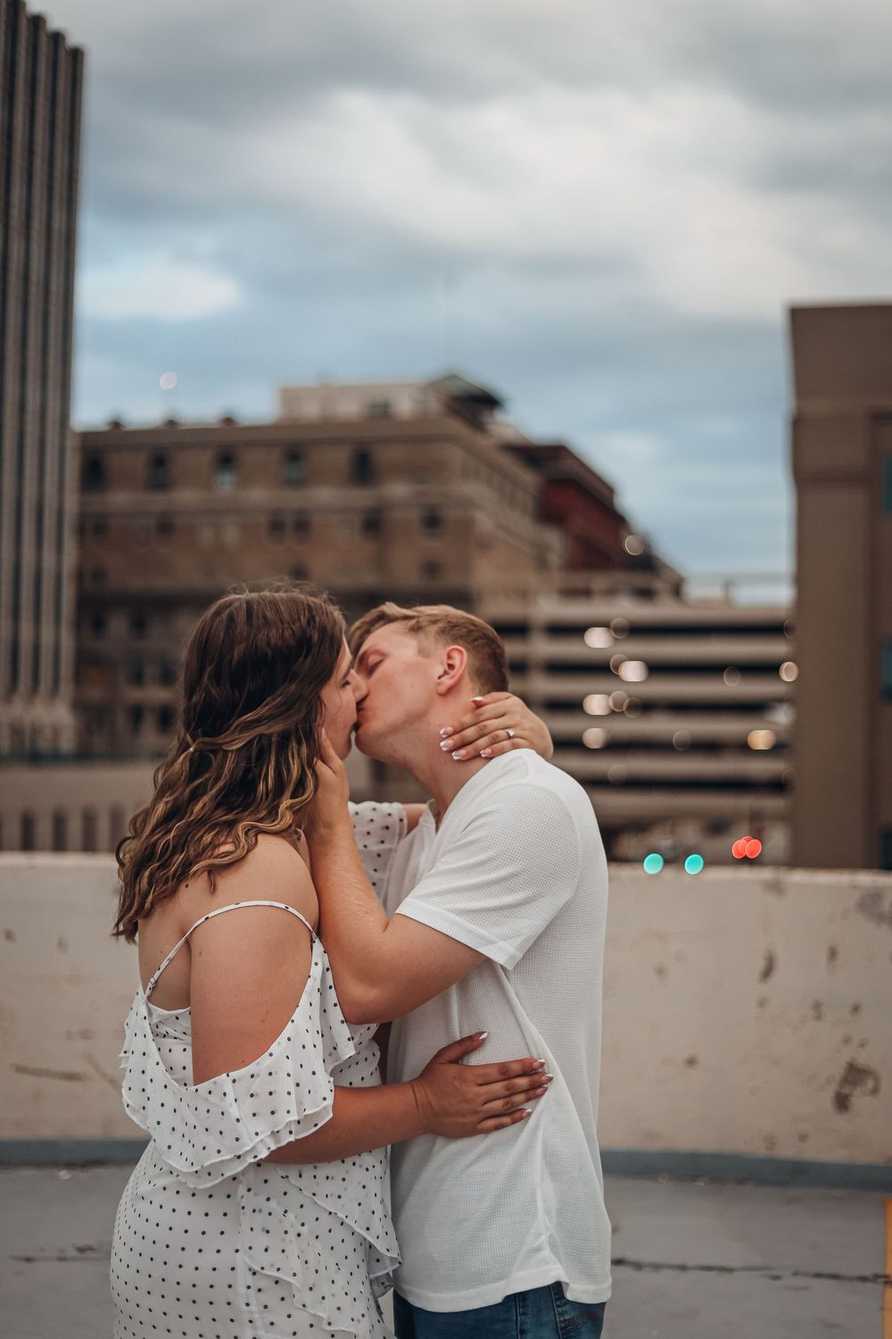 Romantic urban rooftop kiss with city buildings in background. Engagement photography