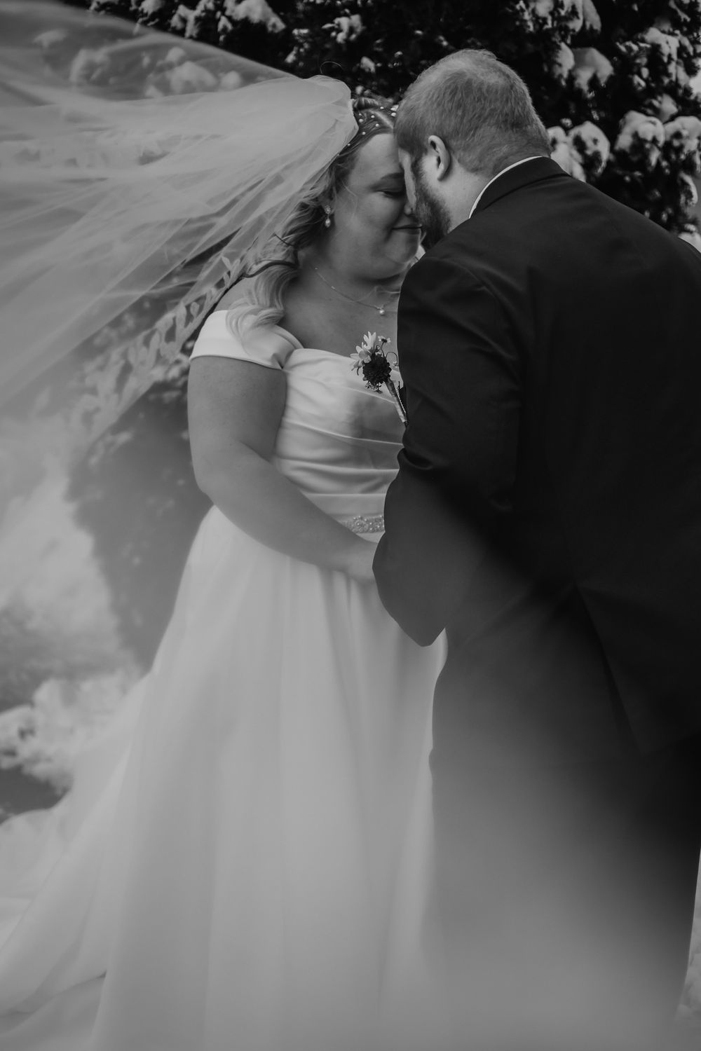 Romantic black and white wedding photo showing couple embracing under snowy trees. Wedding photography