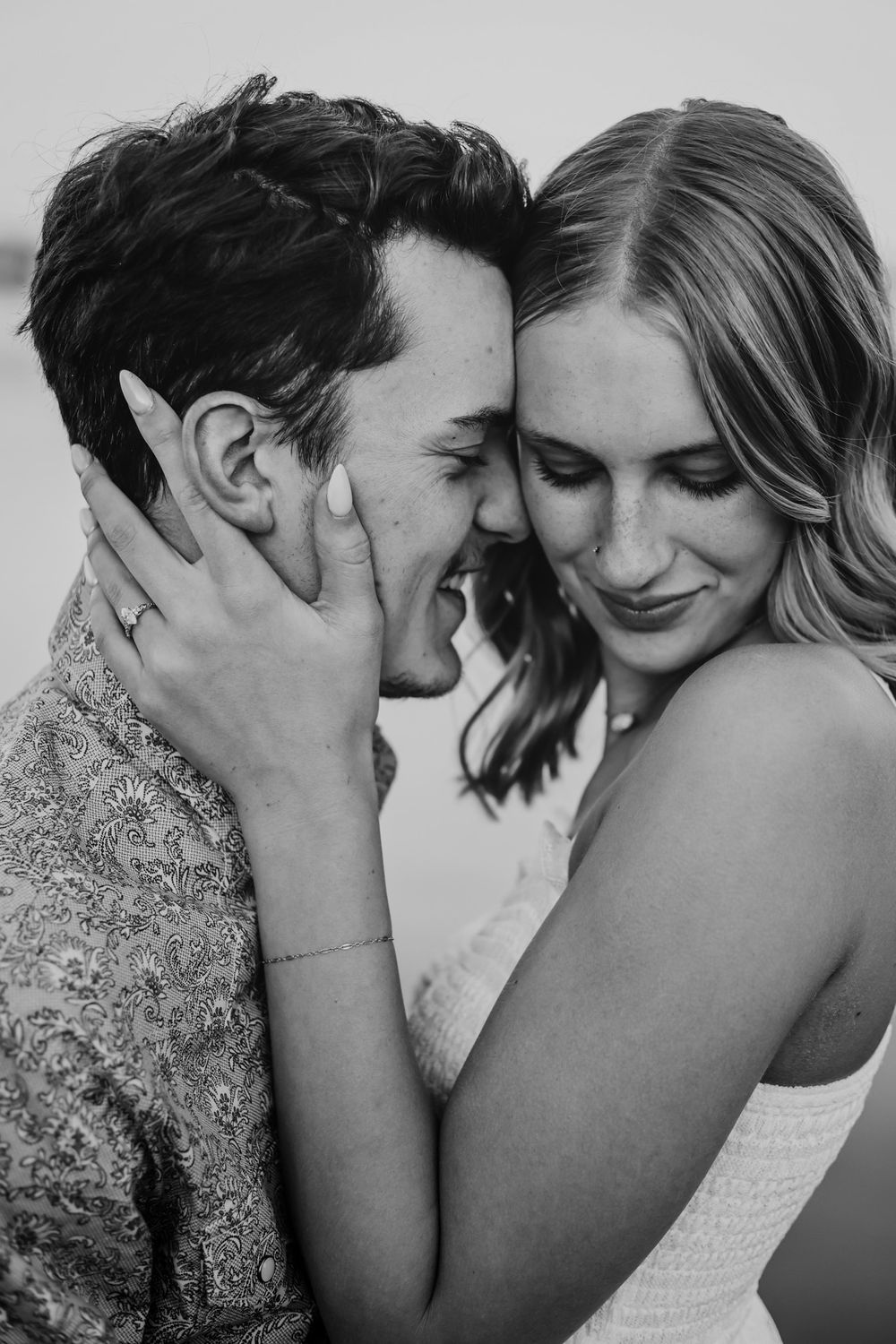 Black and white intimate portrait of a couple sharing a tender romantic moment with their faces close together.
