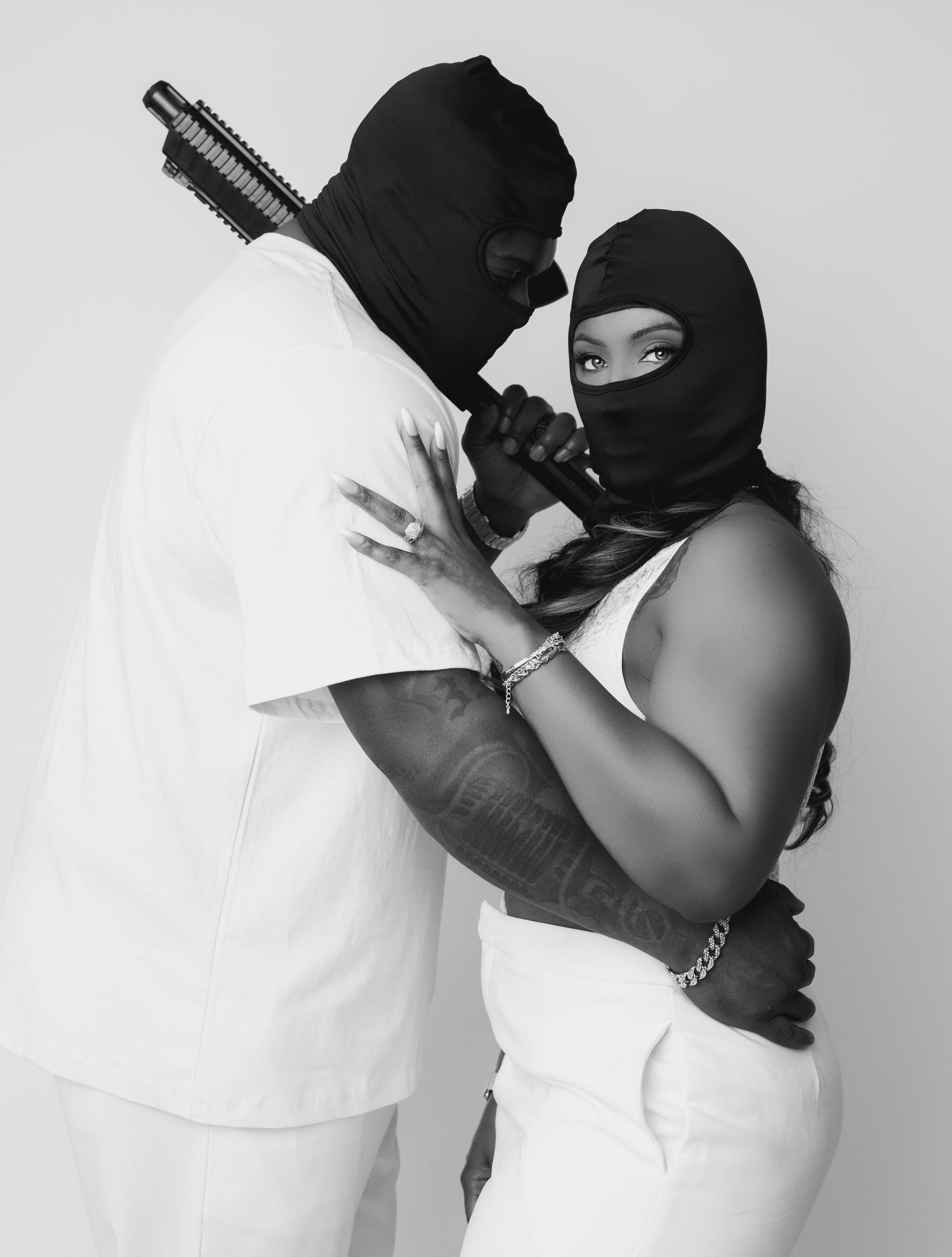Two people in black ski masks embrace in dramatic black and white portrait photography.