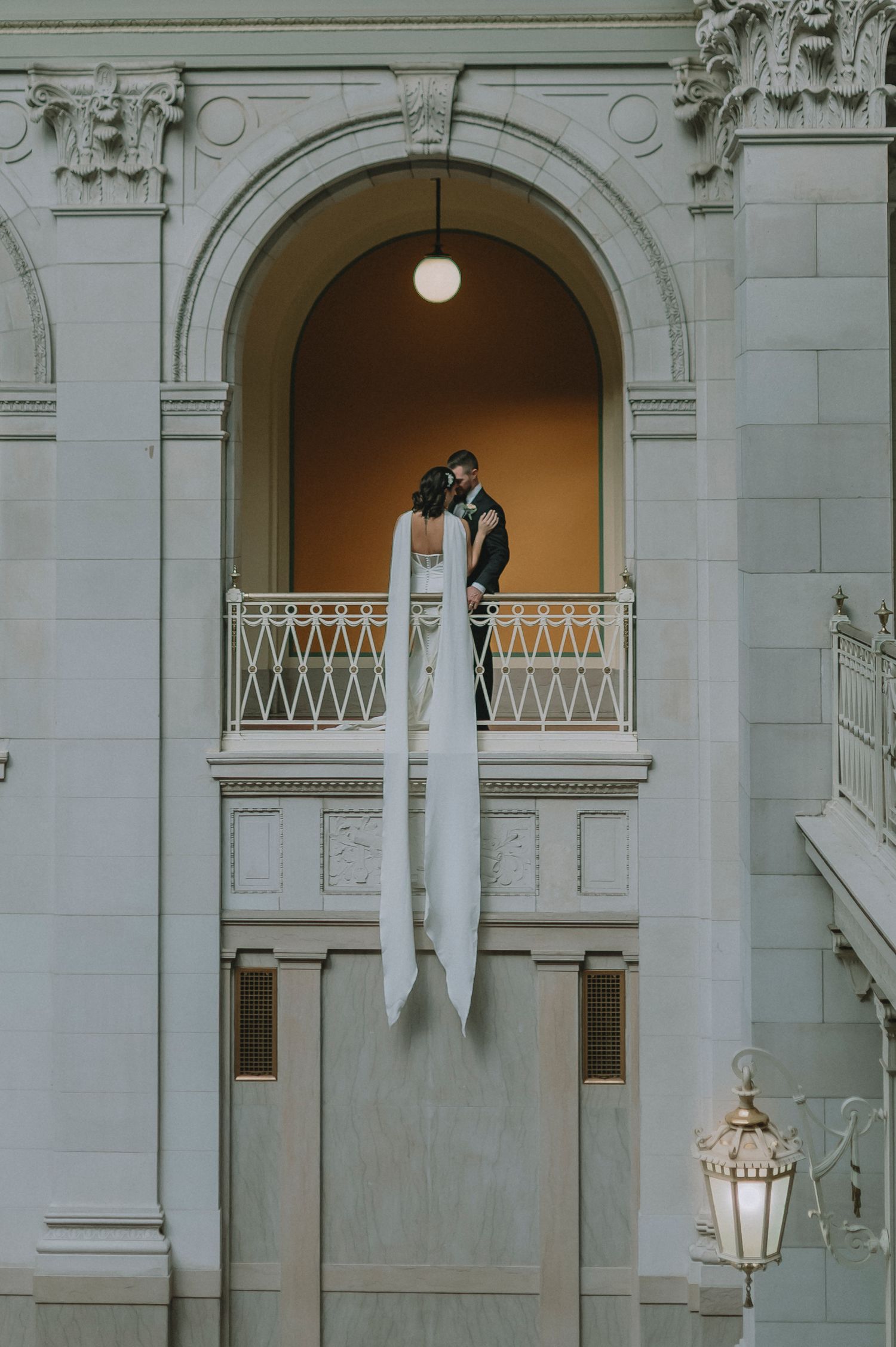 Elegant wedding scene with chandelier and lush greenery in white interior space.