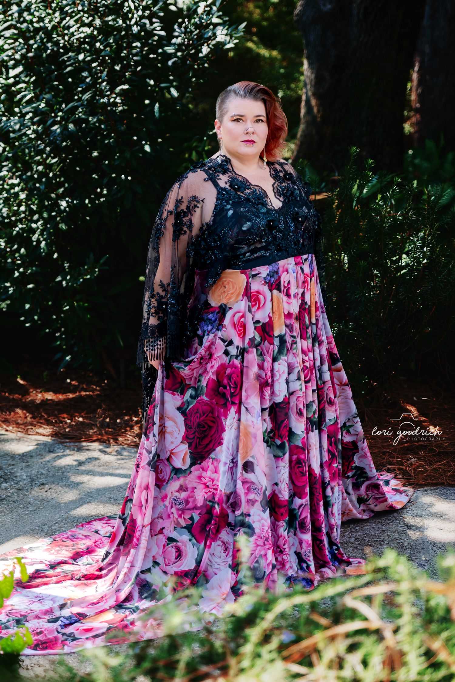 A flowing floral dress with pink and purple tones creates a dramatic silhouette against a wooded outdoor setting.